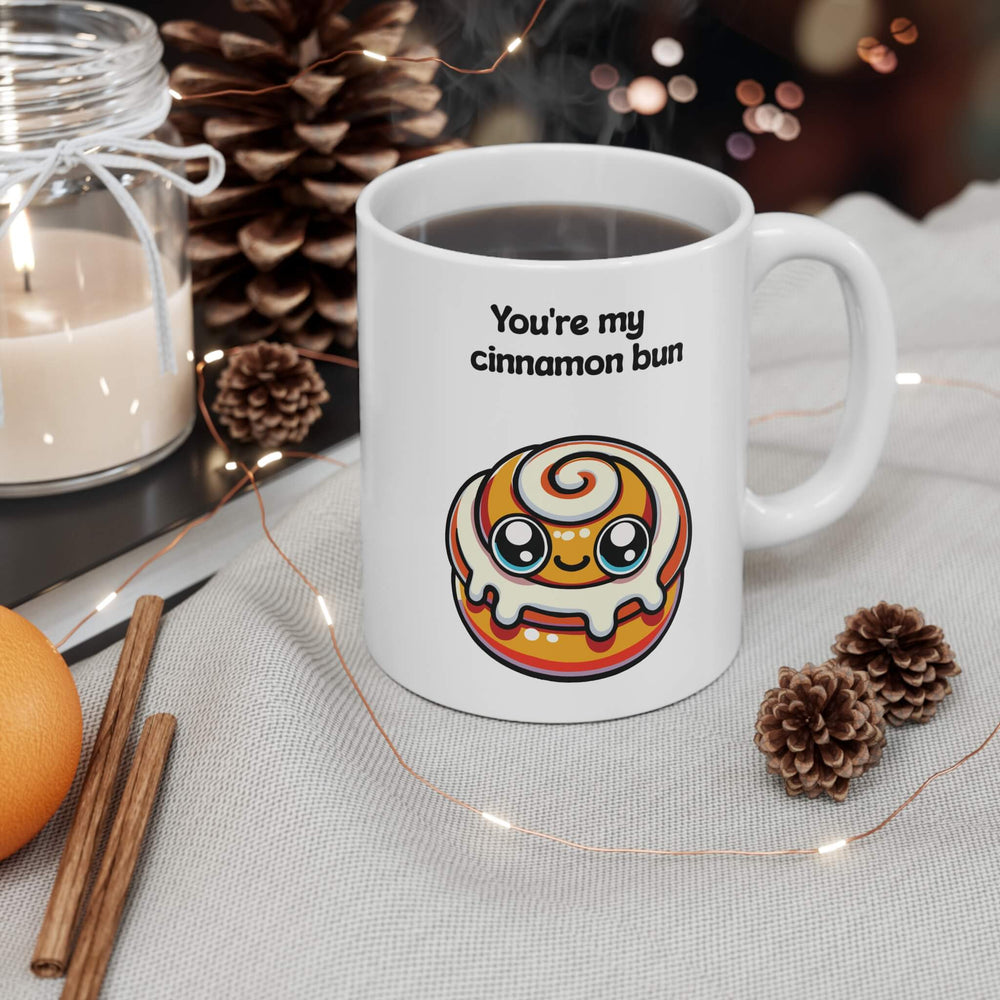 A charming ceramic mug with the phrase "You're my cinnamon bun" and a kawaii-style cinnamon bun illustration, set in a cozy holiday setting with cinnamon sticks and pine cones, enhancing a warm, festive atmosphere.

