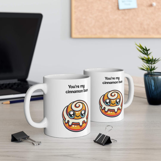 A charming ceramic mug with the phrase "You're my cinnamon bun" and a kawaii-style cinnamon bun illustration, set in a cozy holiday setting with cinnamon sticks and pine cones, enhancing a warm, festive atmosphere.

