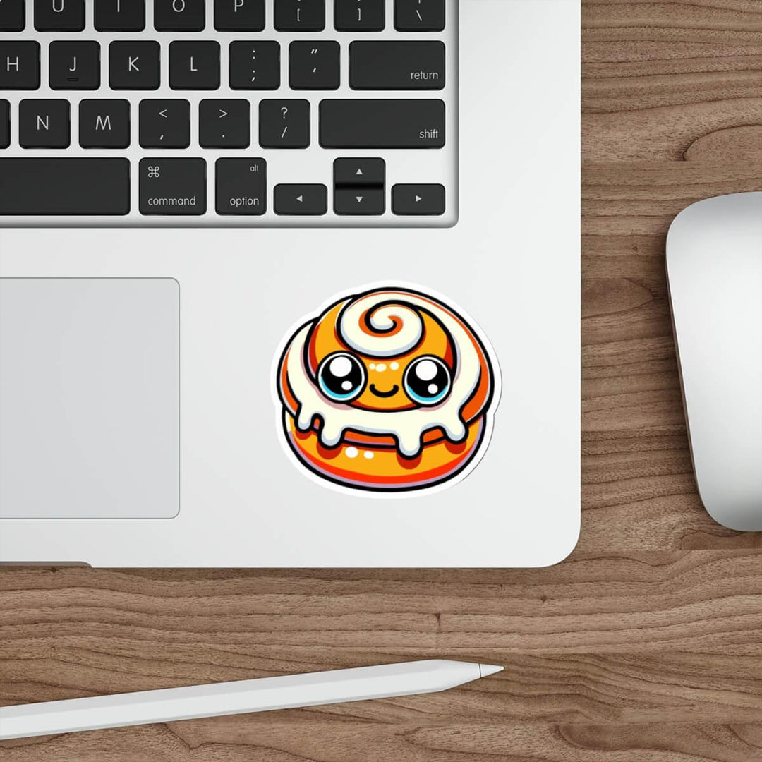 A kawaii-style doughnut sticker with vibrant orange glaze and swirling white icing, placed on a laptop next to a keyboard, embodying a cute and playful aesthetic