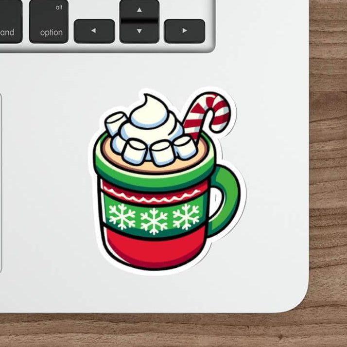 A festive sticker featuring a cozy mug of hot chocolate with whipped cream, marshmallows, and a candy cane, designed in vibrant holiday colors. The sticker is placed on a sleek laptop, showcasing its versatility and cheerful design.