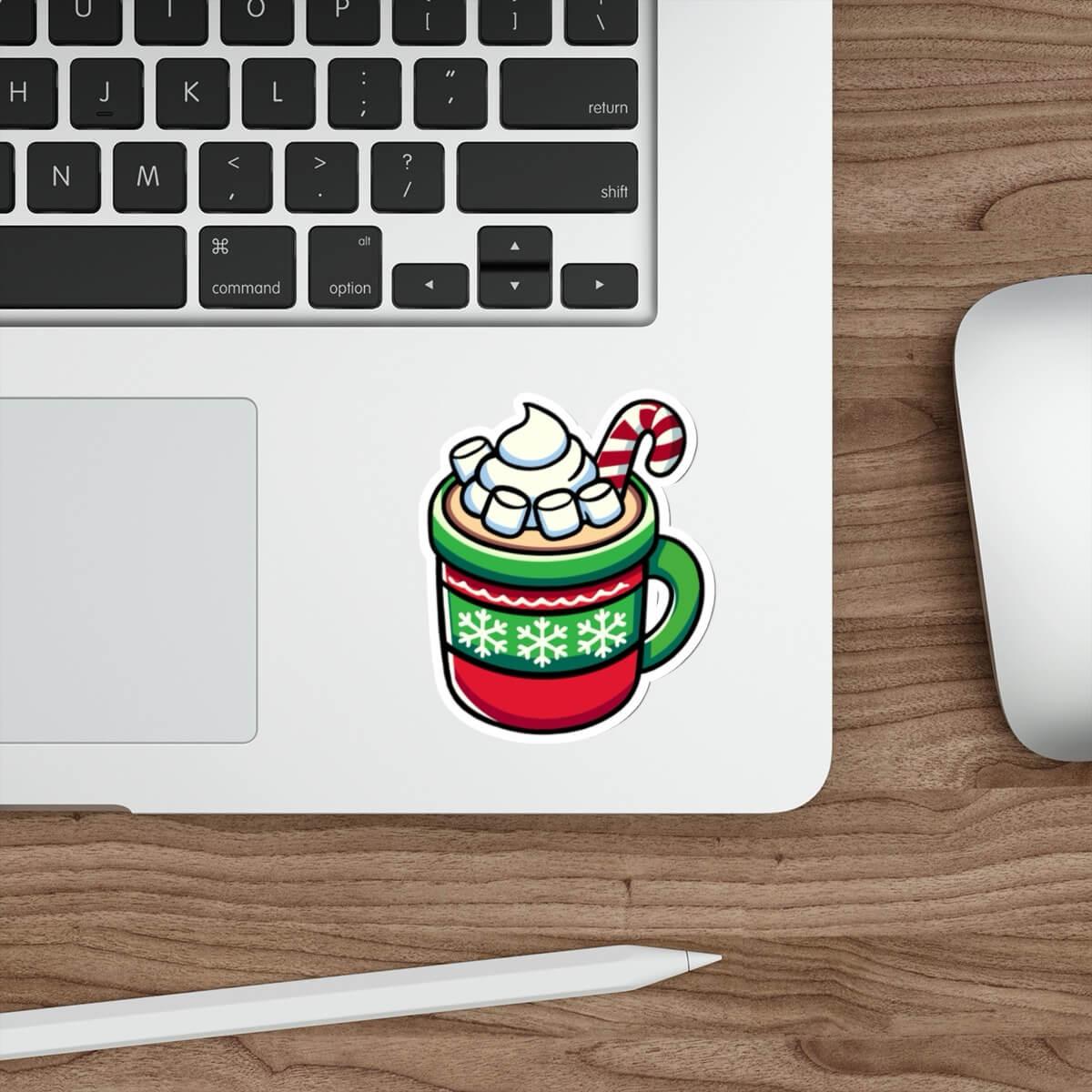 A festive sticker featuring a cozy mug of hot chocolate with whipped cream, marshmallows, and a candy cane, designed in vibrant holiday colors. The sticker is placed on a sleek laptop, showcasing its versatility and cheerful design.