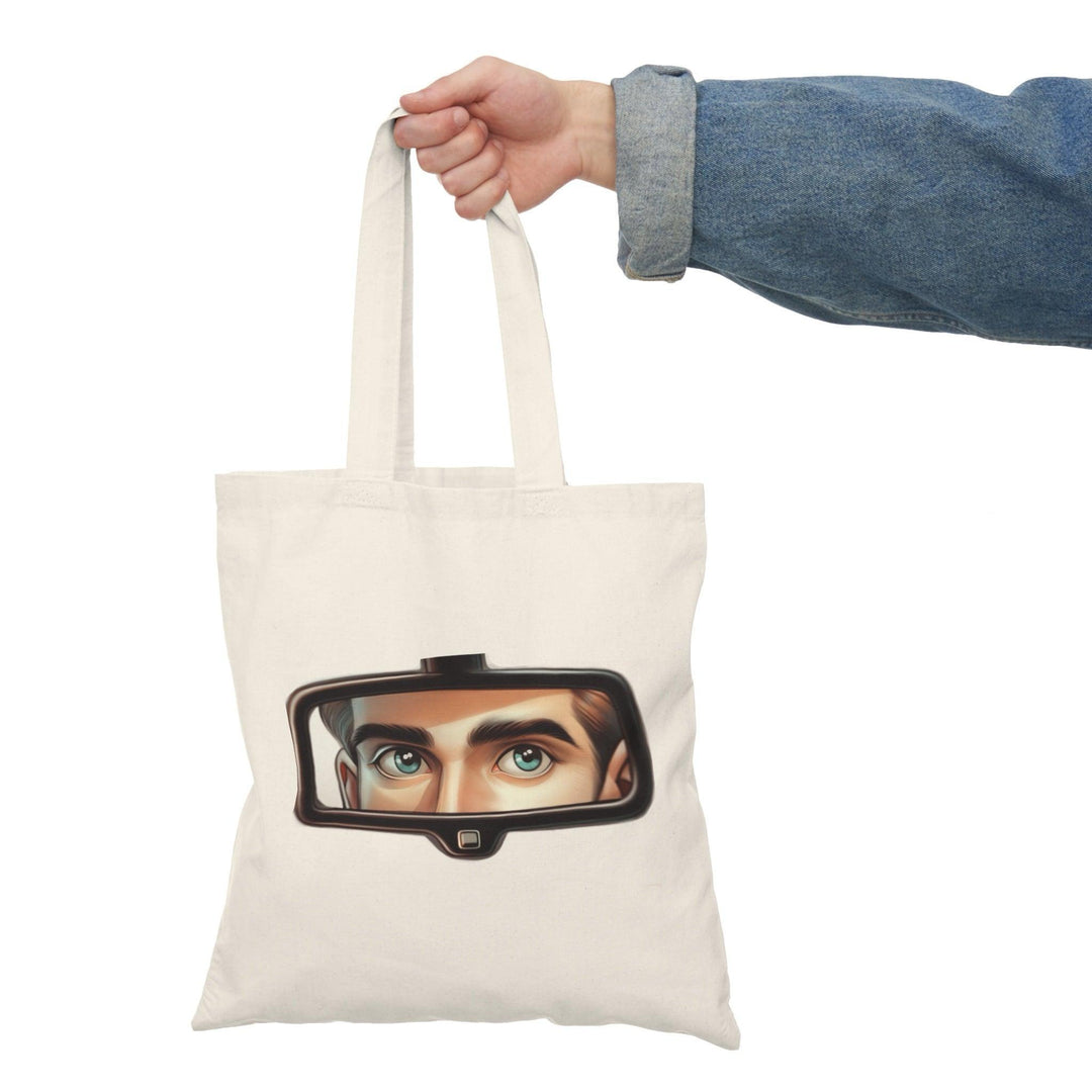 A natural tote bag adorned with a unique design featuring a rearview mirror and eyes peeking through. This intriguing graphic adds an element of mystery and style, making it a standout accessory for those who enjoy creative and artistic designs