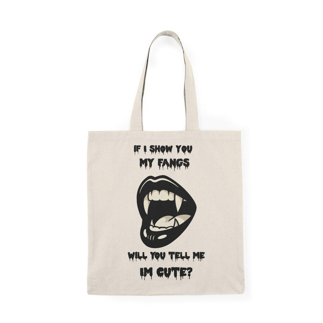 A natural canvas tote bag showcasing a cheeky design with a cartoonish mouth displaying fangs and the text 'If I show you my fangs, will you tell me I'm cute?' The playful combination of humor and confidence makes this tote a great conversation starter."