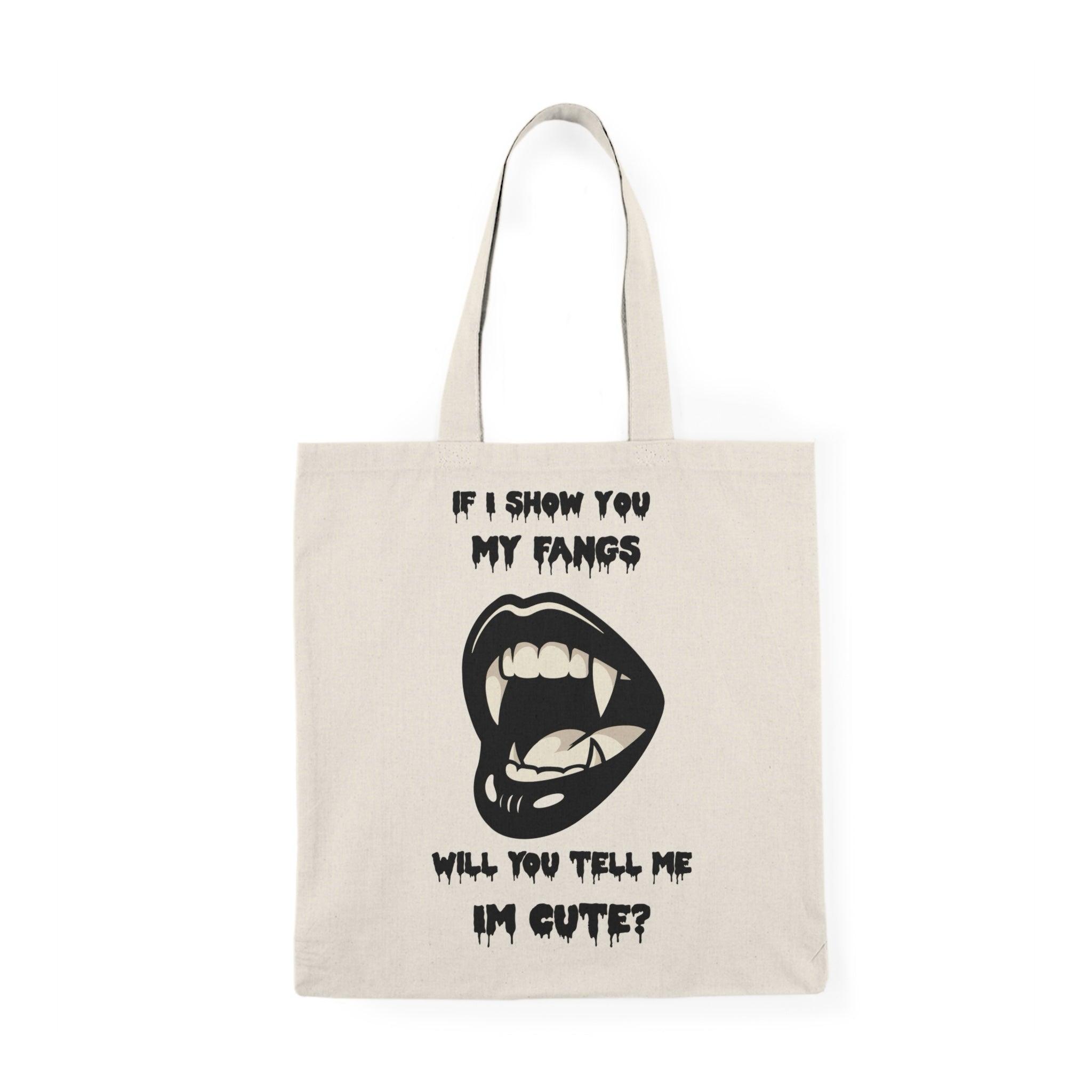 A natural canvas tote bag showcasing a cheeky design with a cartoonish mouth displaying fangs and the text 'If I show you my fangs, will you tell me I'm cute?' The playful combination of humor and confidence makes this tote a great conversation starter."
