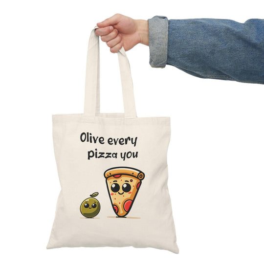 A natural tote bag adorned with a charming graphic of an olive character alongside a slice of pizza and the text 'Olive every pizza you.' The punny design adds a delightful touch to this bag, making it a fun choice for pizza lovers and food enthusiasts