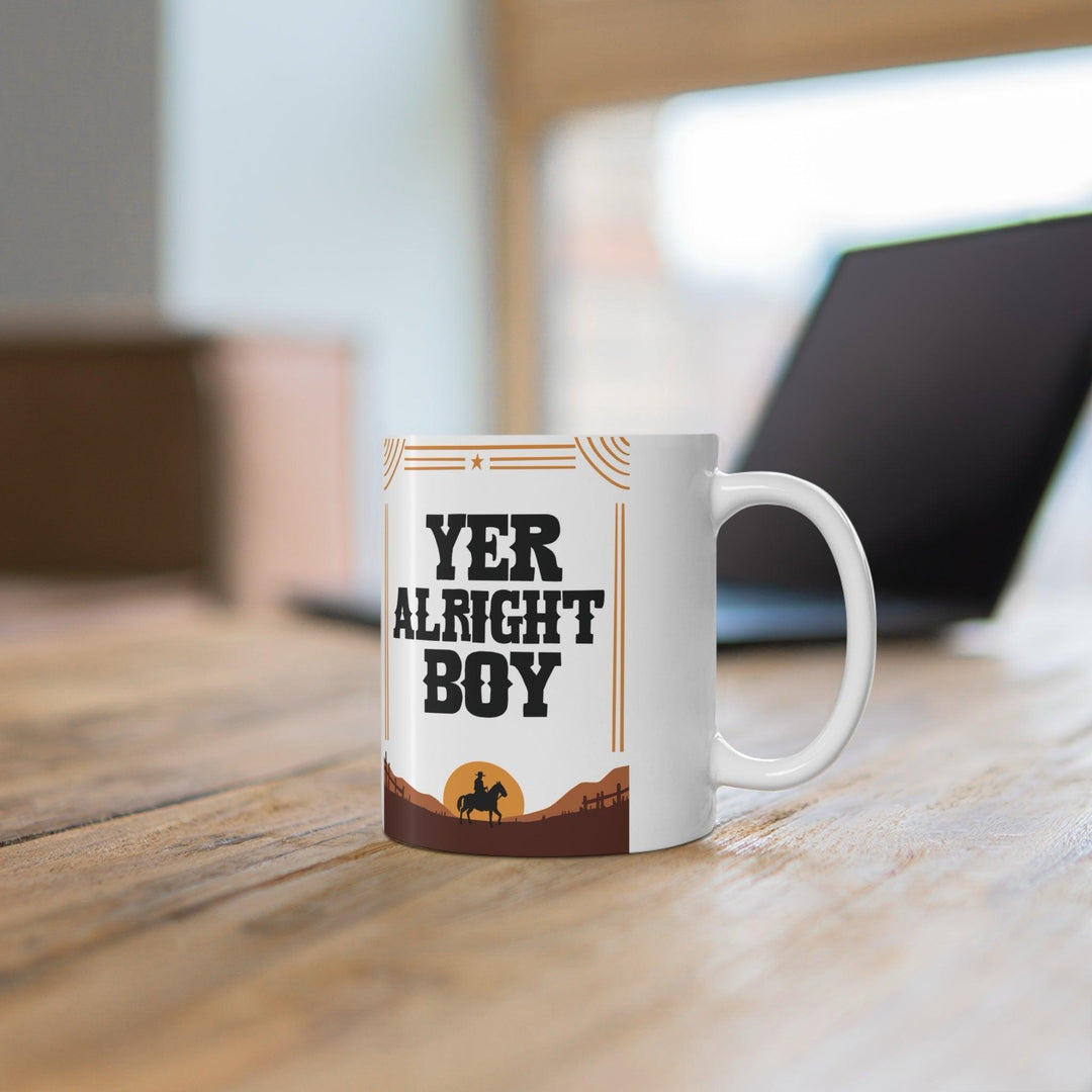 Playful ceramic mug featuring the phrase 'Yer Alright Boy' against a desert scene. A fun gift for friends or family, perfect for morning coffee or tea - Baby Keo