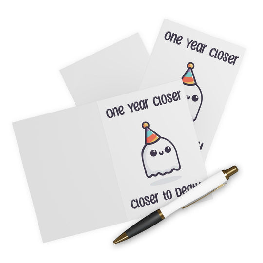 Funny and slightly dark birthday card featuring a smiling ghost in a party hat with the phrase 'One Year Closer to Death.' Ideal for friends with a morbid sense of humor who appreciate sarcastic cards - Baby Keo.