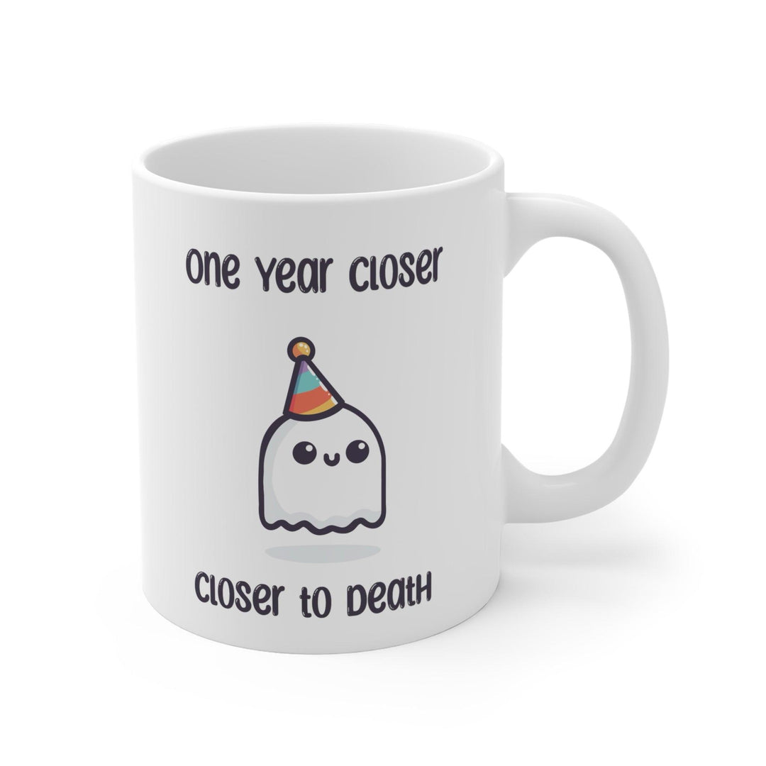 White ceramic mug featuring a ghost illustration and the darkly humorous text 'One Year Closer to Death,' perfect for those who enjoy a bit of morbid humor