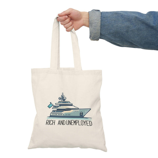 A cream-colored tote bag featuring a humorous design with the text 'Rich and Unemployed' alongside an illustration of a luxury yacht. This playful graphic contrasts wealth with unemployment, making it a fun accessory for those who appreciate irony.