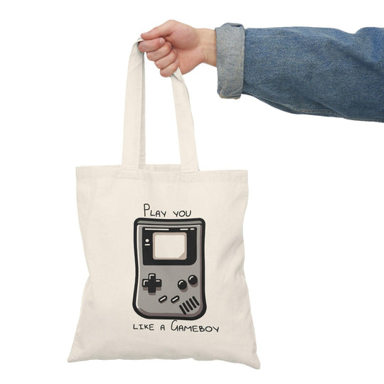 A cream tote bag featuring a retro Gameboy graphic with the phrase 'Play you like a Gameboy' in a fun font. This nostalgic design appeals to gaming enthusiasts and adds a playful touch to everyday accessories.