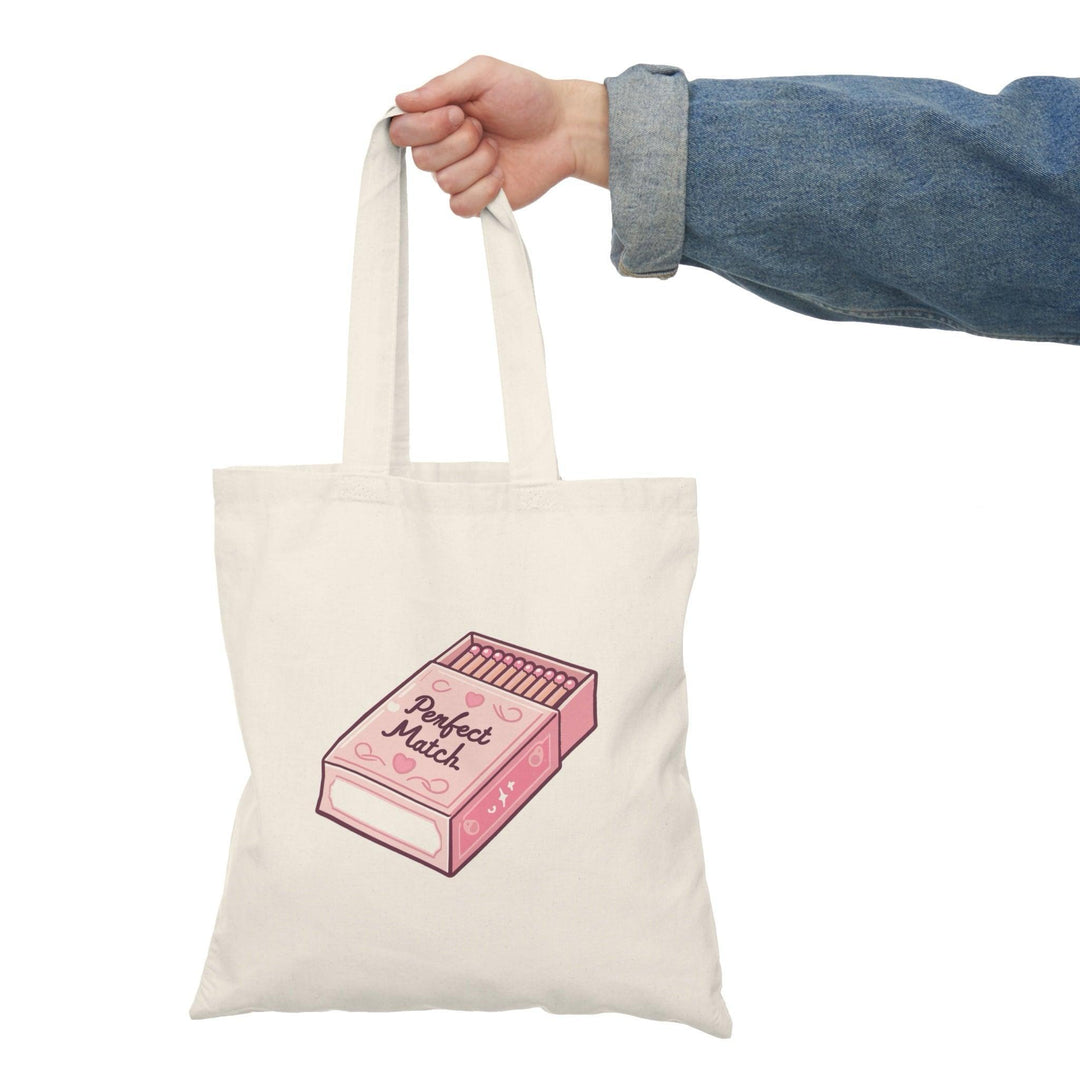 A cream tote bag featuring an artistic illustration of a matchbox with the phrase 'Perfect Match' written in a stylish font. The creative design gives a nod to love and connection, making it an ideal gift for couples or those who appreciate clever graphics