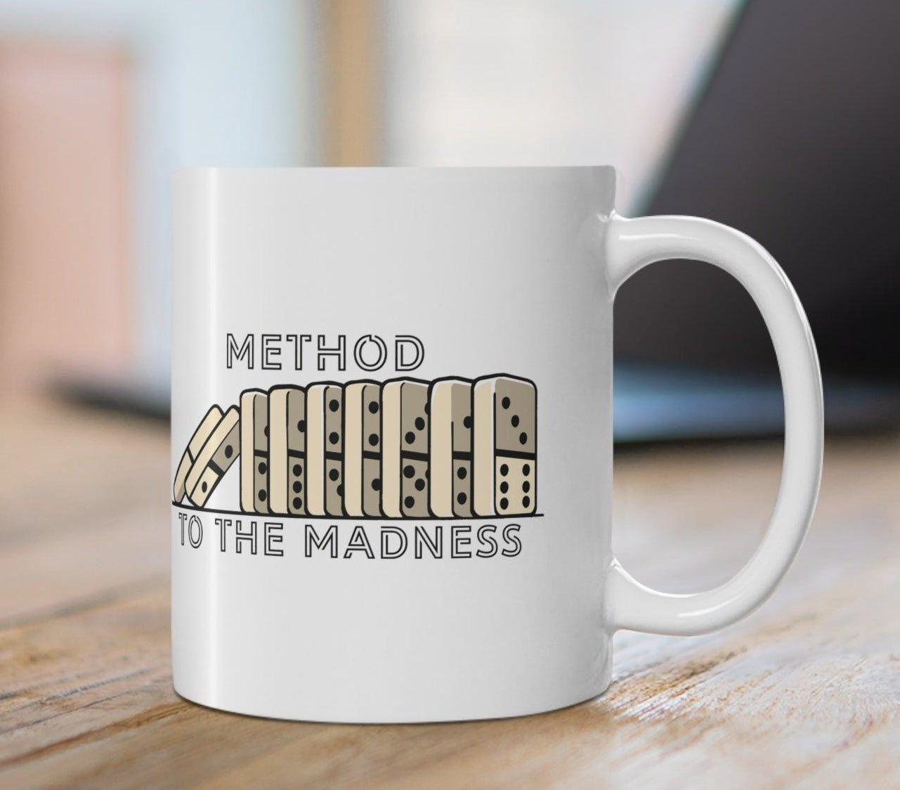 A white ceramic mug with a text and domino pattern design placed on a wooden table.