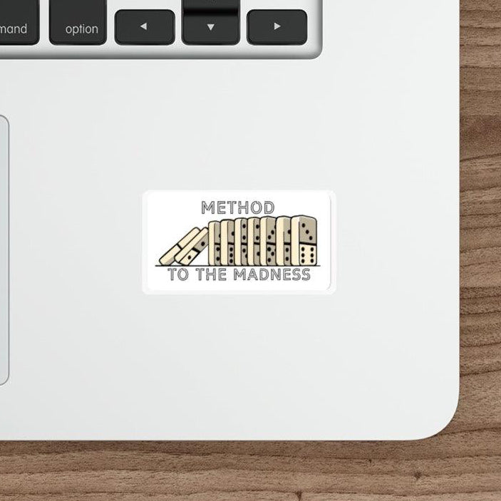 A sticker with the text 'METHOD TO THE MADNESS' and an illustration of falling dominos placed on a laptop.