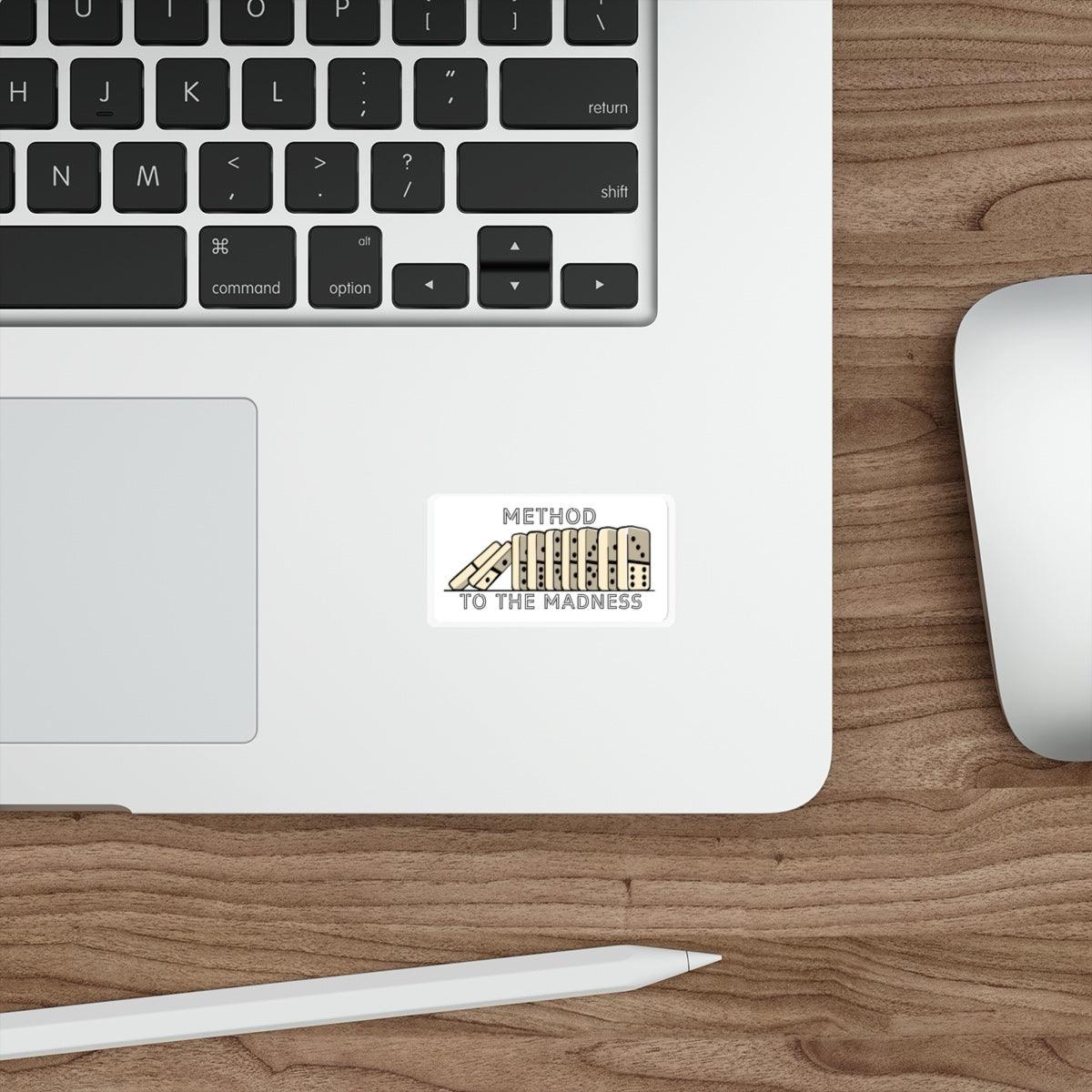 A sticker with the text 'METHOD TO THE MADNESS' and an illustration of falling dominos placed on a laptop.