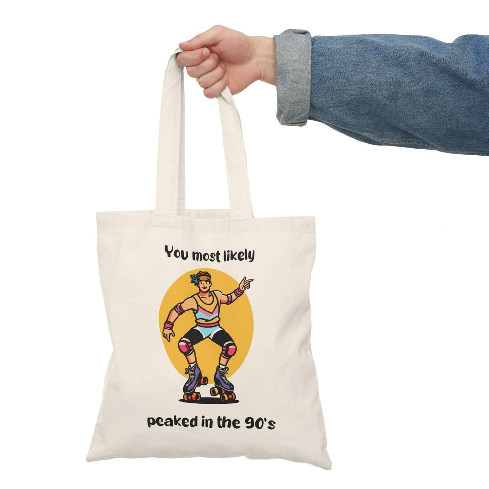 A cream tote bag showcasing a colorful graphic of a character with the text 'You Most Likely Peaked in the 90's.' The nostalgic design resonates with those who appreciate the fun and style of the 90s, adding a playful touch to any outfit.