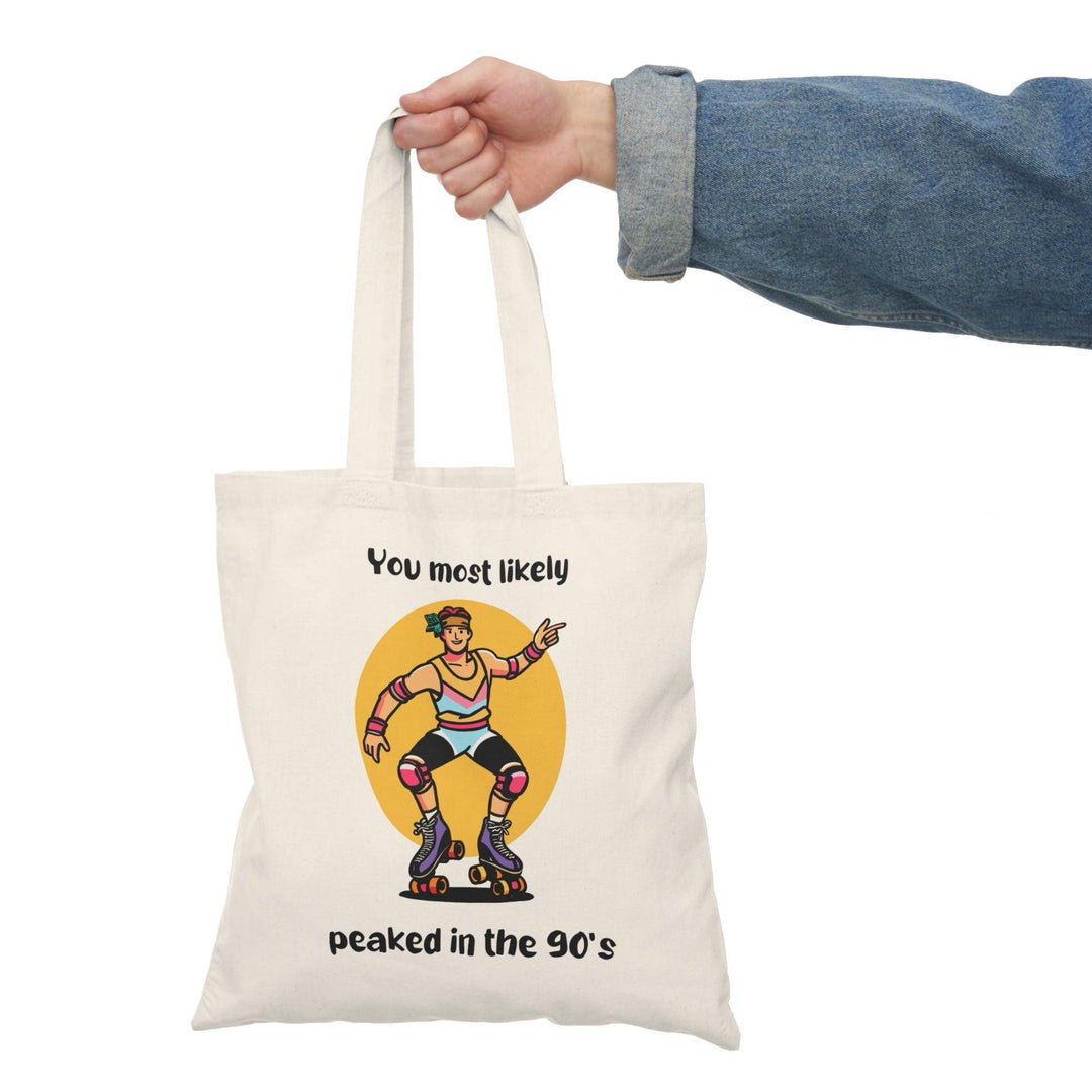 A cream tote bag showcasing a colorful graphic of a character with the text 'You Most Likely Peaked in the 90's.' The nostalgic design resonates with those who appreciate the fun and style of the 90s, adding a playful touch to any outfit.