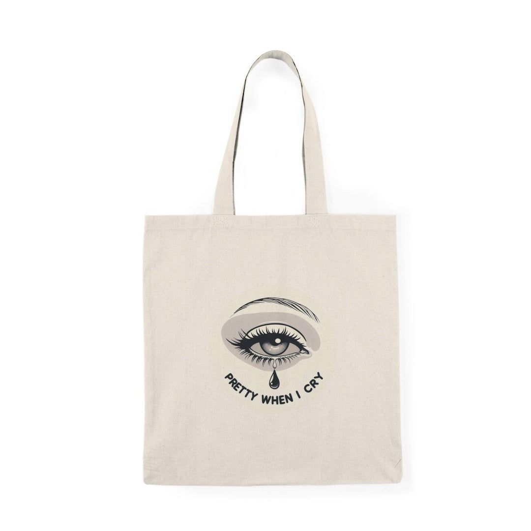 A natural canvas tote bag showcasing an artistic graphic of a teardrop with the phrase 'Pretty When I Cry.' The thoughtful design combines emotion with beauty, appealing to those who embrace vulnerability and self-expression