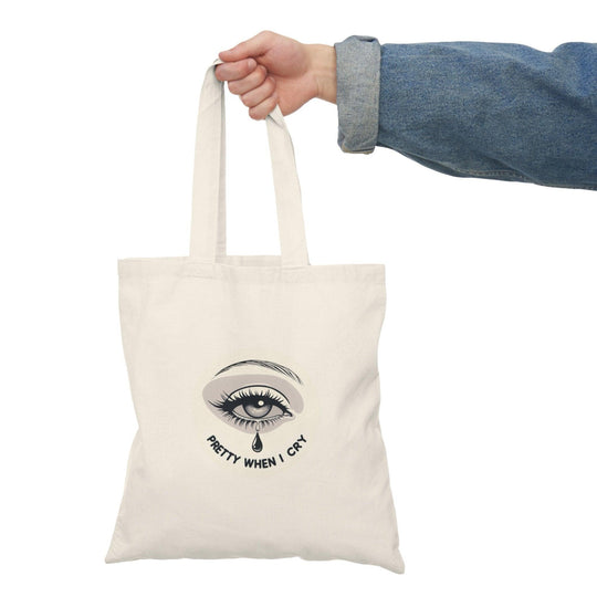 A natural canvas tote bag showcasing an artistic graphic of a teardrop with the phrase 'Pretty When I Cry.' The thoughtful design combines emotion with beauty, appealing to those who embrace vulnerability and self-expression