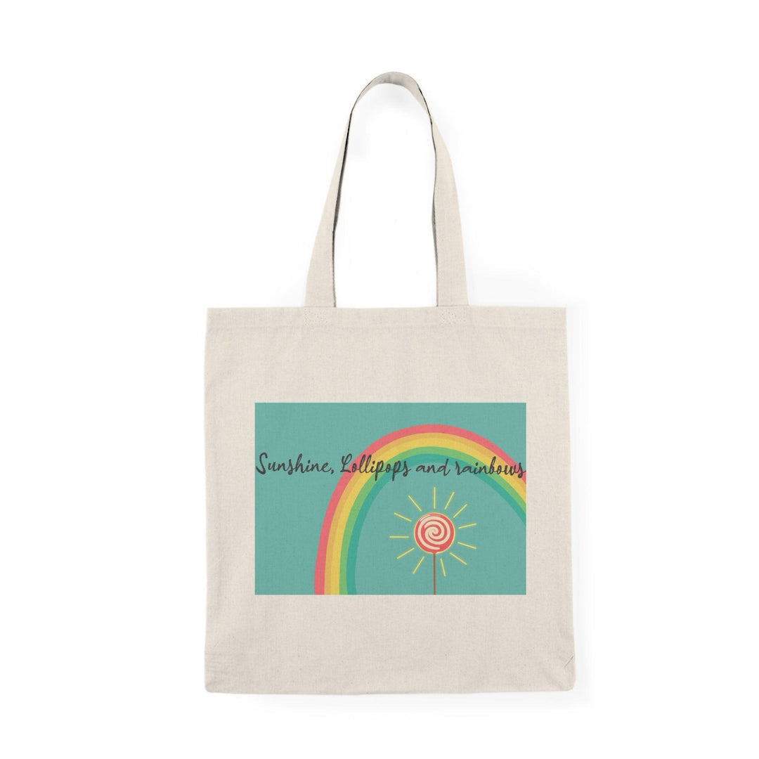 A cream tote bag adorned with a colorful graphic featuring a rainbow, lollipops, and sunshine with the text 'Sunshine, Lollipops and Rainbows.' This cheerful design radiates positivity and happiness, making it a delightful accessory for brightening up any day."