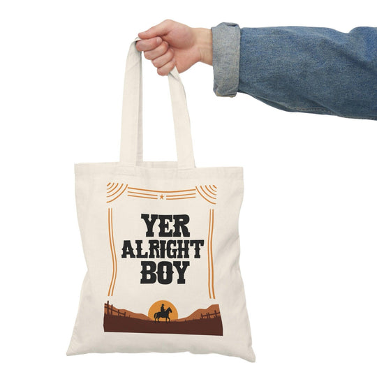 A natural tote bag with bold typography stating 'Yer Alright Boy,' accompanied by a graphic of a landscape. This fun design adds a lighthearted, friendly touch, making it perfect for those with a charming sense of humor