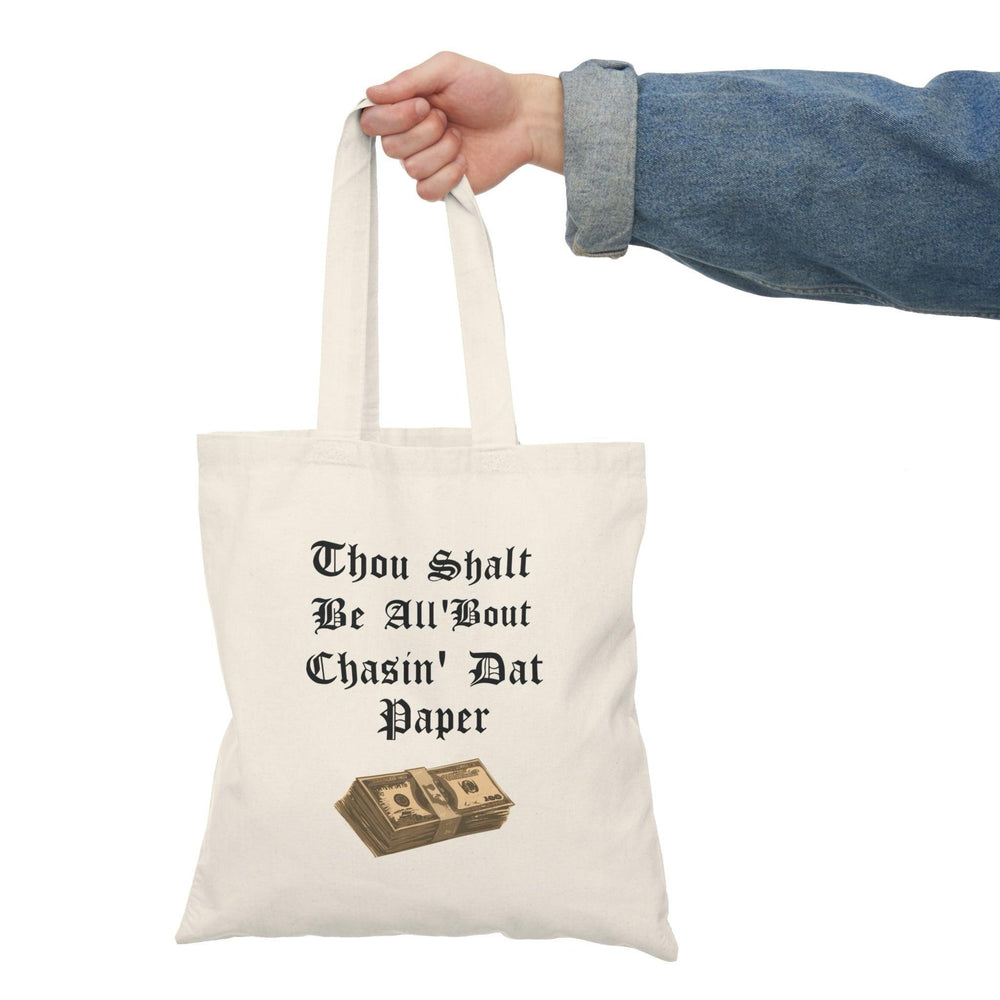 A cream tote bag featuring a stylish design with the phrase 'Thou Shalt Be All 'Bout Chasin' Dat Paper' in an eye-catching font. This fun and motivational message appeals to those who are ambitious and driven, adding a touch of humor to daily life