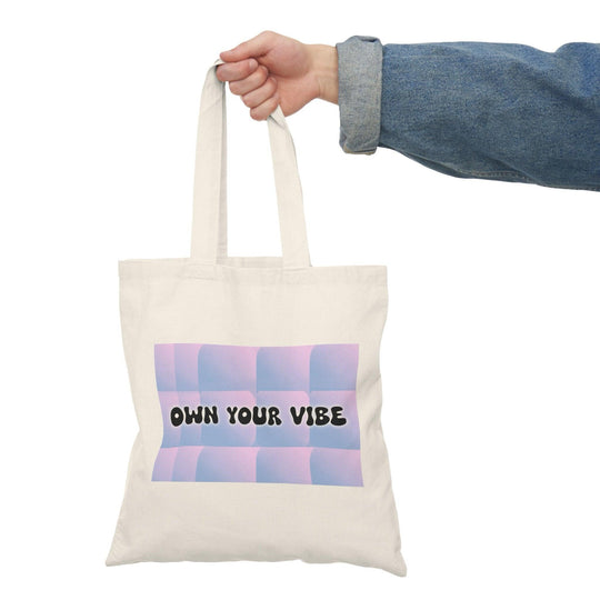 A natural tote bag showcasing the text 'Own Your Vibe' in a modern, stylish font against a gradient background. The design encourages positivity and self-expression, making it an uplifting addition to any outfit