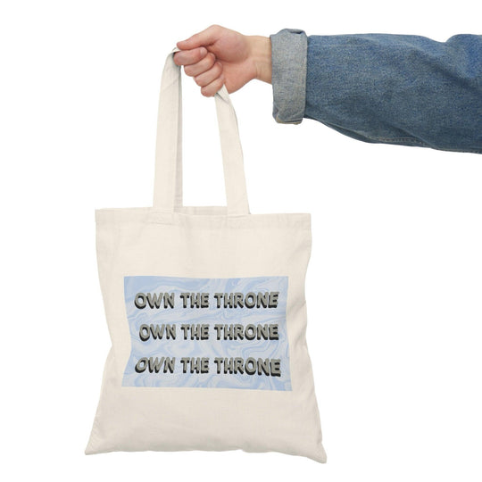 A cream tote bag featuring the phrase 'Own The Throne' repeated in a stylish and colorful font. The vibrant colors and eye-catching design inspire confidence and empowerment, making it a great accessory for those who want to make a statement