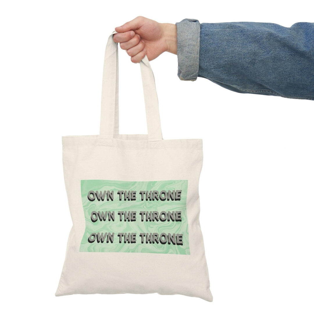 A cream tote bag featuring the phrase 'Own The Throne' repeated in a stylish and colorful font. The vibrant colors and eye-catching design inspire confidence and empowerment, making it a great accessory for those who want to make a statement