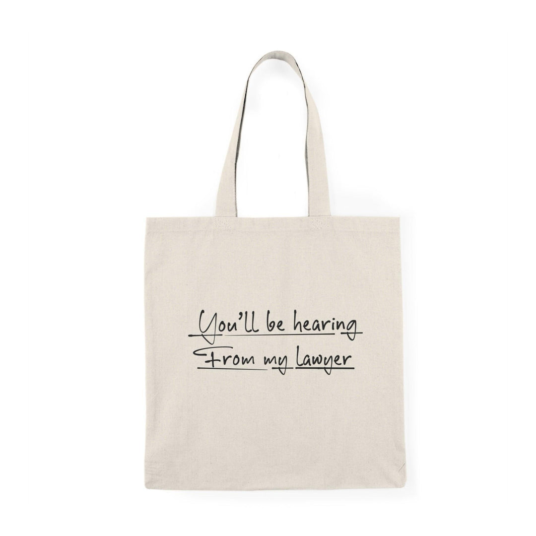 A cream-colored tote bag featuring a playful design with the text 'You'll be hearing from my lawyer.' The bold typography adds a humorous touch, making it a fun accessory for anyone who appreciates witty legal humor.