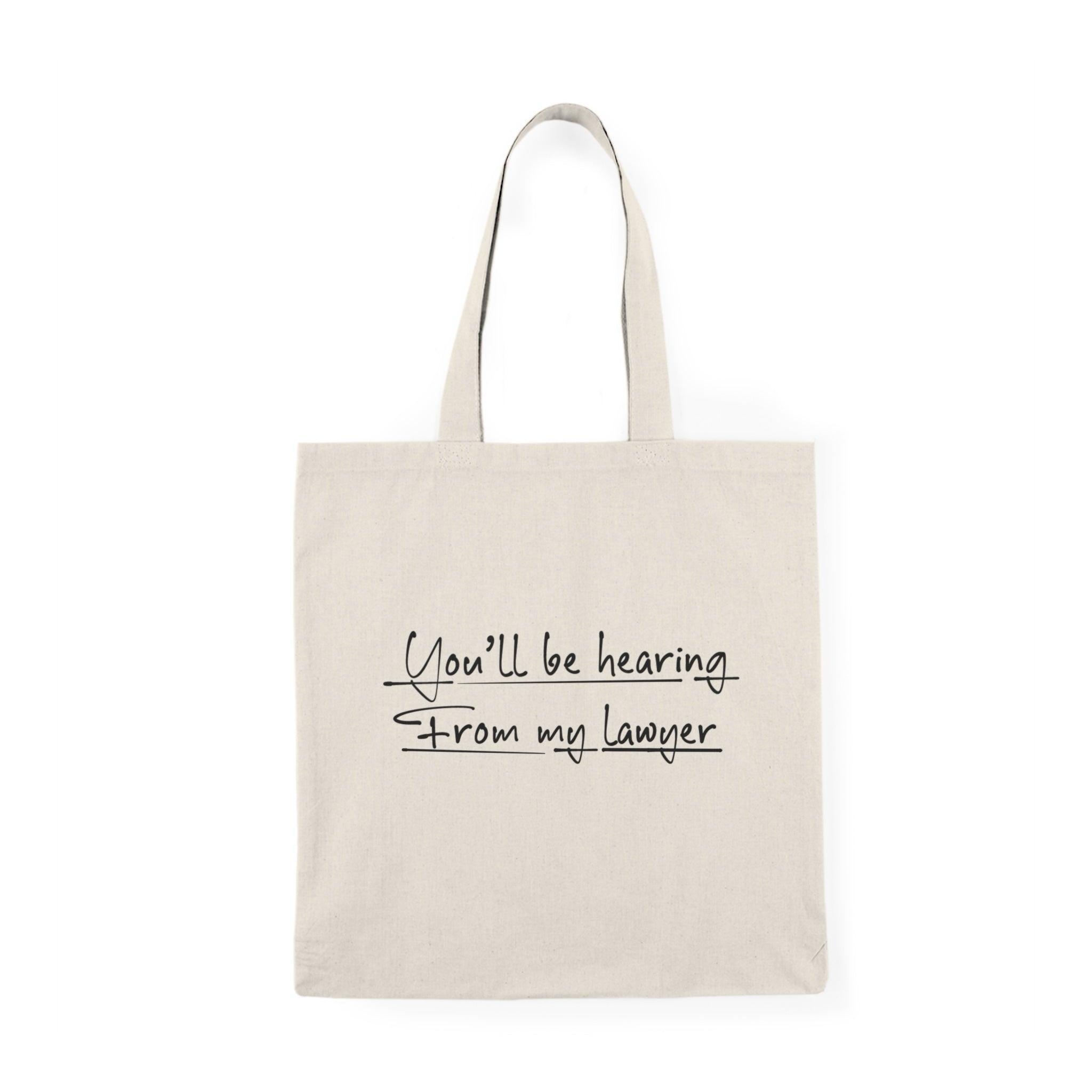 A cream-colored tote bag featuring a playful design with the text 'You'll be hearing from my lawyer.' The bold typography adds a humorous touch, making it a fun accessory for anyone who appreciates witty legal humor.