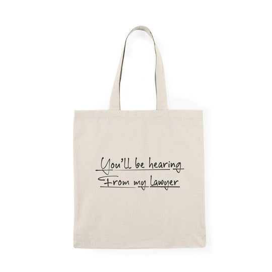 A cream-colored tote bag featuring a playful design with the text 'You'll be hearing from my lawyer.' The bold typography adds a humorous touch, making it a fun accessory for anyone who appreciates witty legal humor.
