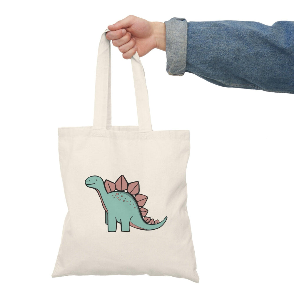 Tote bag featuring a fun and colorful illustration of a cheerful dinosaur, complete with vibrant scales and a playful expression. The whimsical design adds a touch of prehistoric charm, making it an ideal accessory for dinosaur enthusiasts and anyone looking to express their playful personality in everyday carry."