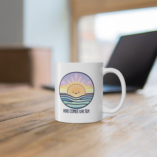 White ceramic mug with a cheerful sun illustration and the positive phrase 'Here Comes the Sun,' ideal for starting the day with a smile
