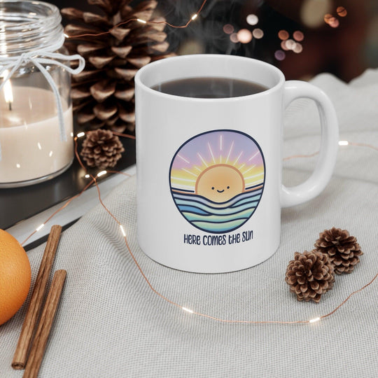 White ceramic mug with a cheerful sun illustration and the positive phrase 'Here Comes the Sun,' ideal for starting the day with a smile