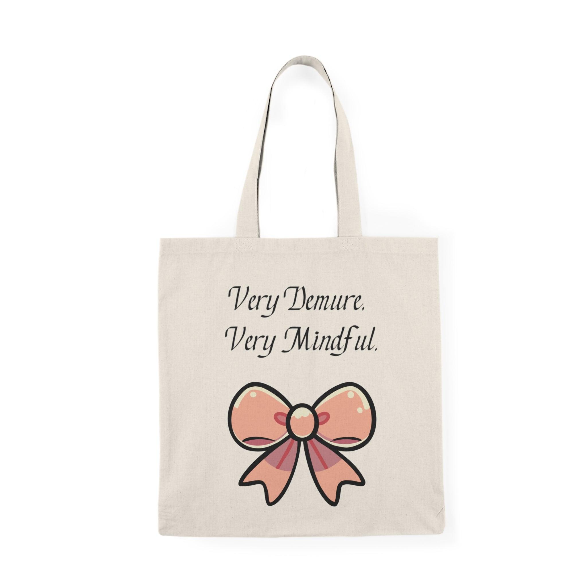 A cream tote bag adorned with a stylish design featuring the phrase 'Very Demure. Very Mindful.' paired with a decorative bow graphic. This elegant design resonates with those who appreciate a sense of calm and mindfulness in their lives