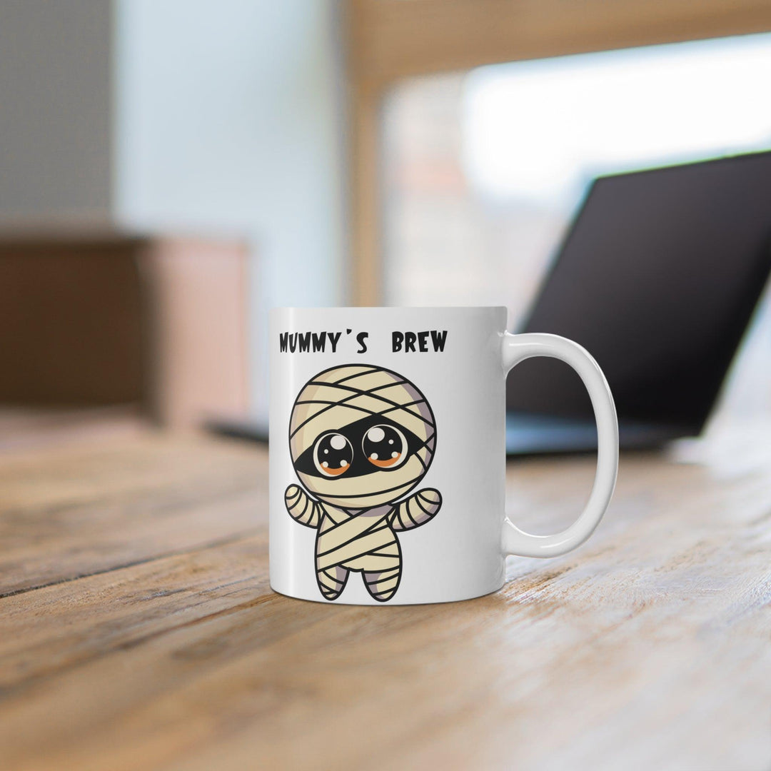 Fun white ceramic mug featuring a cartoon mummy with the playful text 'Mummy’s Brew,' perfect for Halloween or spooky coffee moments.