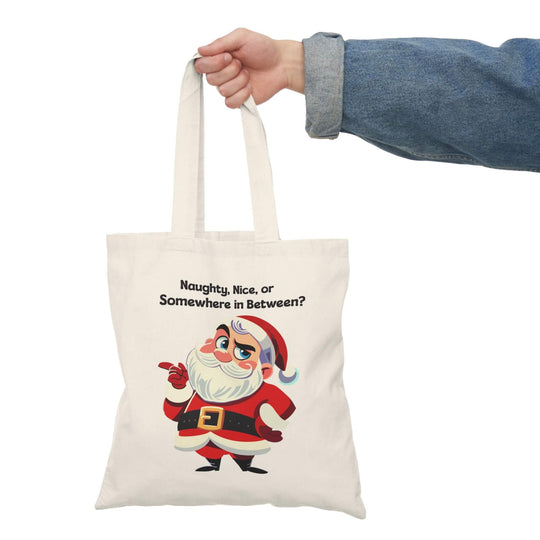 Cheeky Santa tote bag with the phrase 'Naughty, Nice, or Somewhere in Between?' Perfect for holiday shopping or as a festive accessory. Made from 100% recycled cotton, measuring 40 x 38 cm (15.7 x 15 inches) and 130-135 gsm thickness, this eco-friendly tote is durable and adds a playful touch to the season.