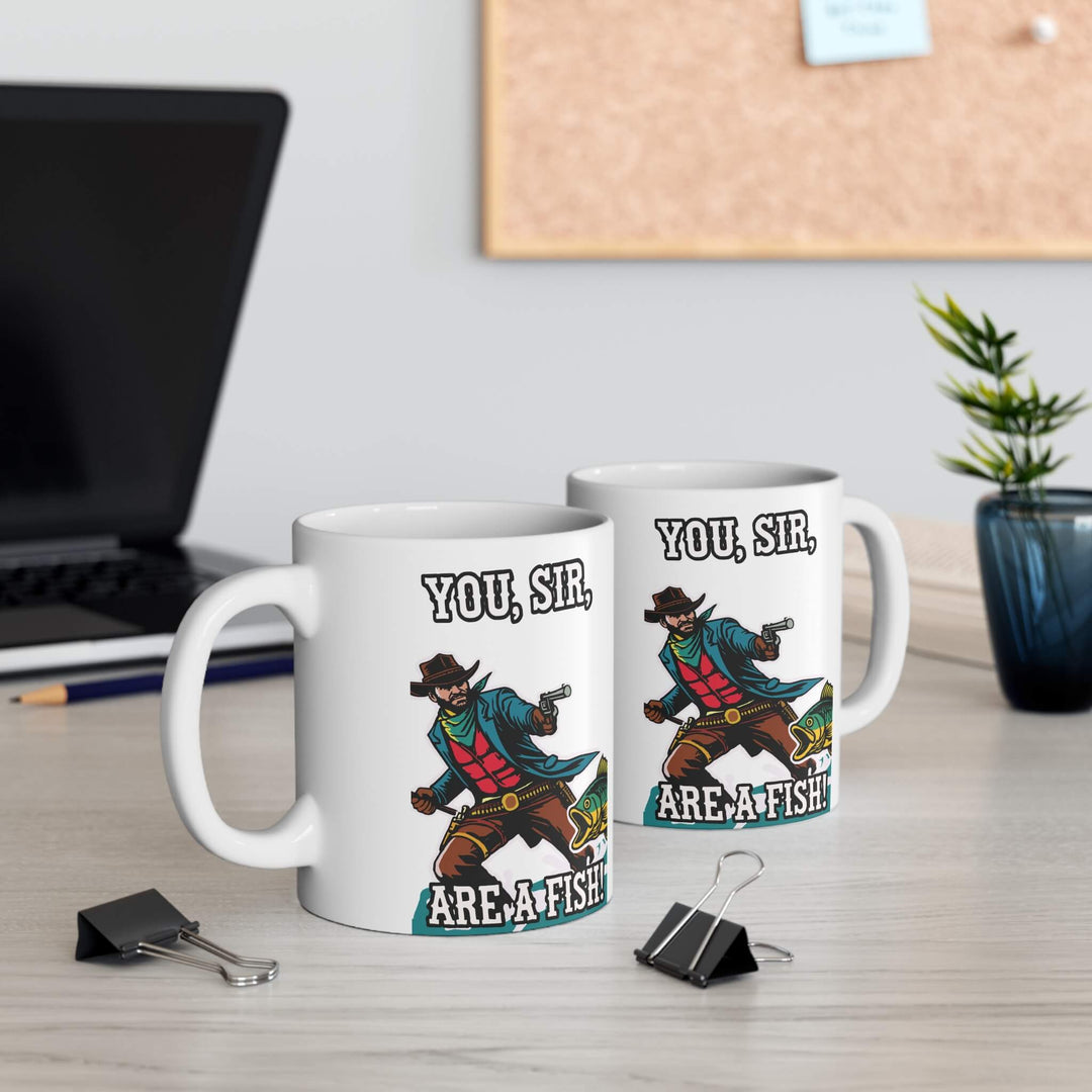 A humorous 11oz ceramic mug featuring a vibrant design of a cowboy aiming at a fish with the text "You, Sir, Are a Fish!" Perfect for coffee lovers with a quirky sense of humor, featuring a glossy finish, microwave and dishwasher-safe.