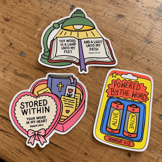 Three colorful die-cut stickers featuring Bible verses and religious illustrations, arranged on a wooden tabletop. The stickers include a lamp-shaped design with Psalm 119:10, a heart-shaped box design with Psalm 119:11, and a battery-card design with Hebrews 4:12.