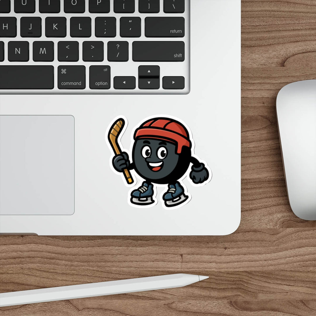 Vinyl sticker of a cartoon hockey puck character with a red helmet and skates, shown on a silver laptop near a keyboard.