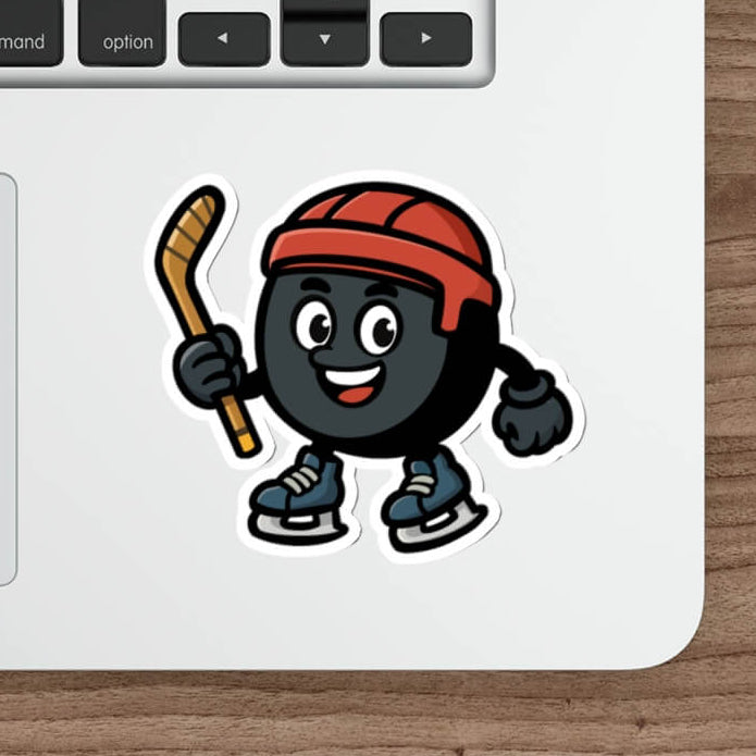 Vinyl sticker of a cartoon hockey puck character with a red helmet and skates, shown on a silver laptop near a keyboard.