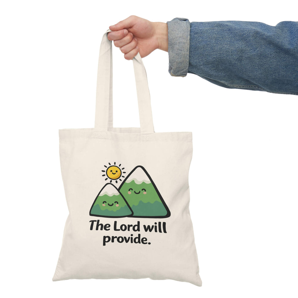 Tote bag with mountains and sun design and 'The Lord will provide' text, held by a person.