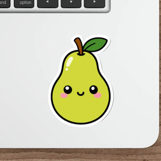 A cute cartoon pear sticker with a smiling face and green leaf, applied to the lower part of a silver laptop keyboard. The laptop is shown on a wooden desk alongside a white mouse, stylus, and keyboard.