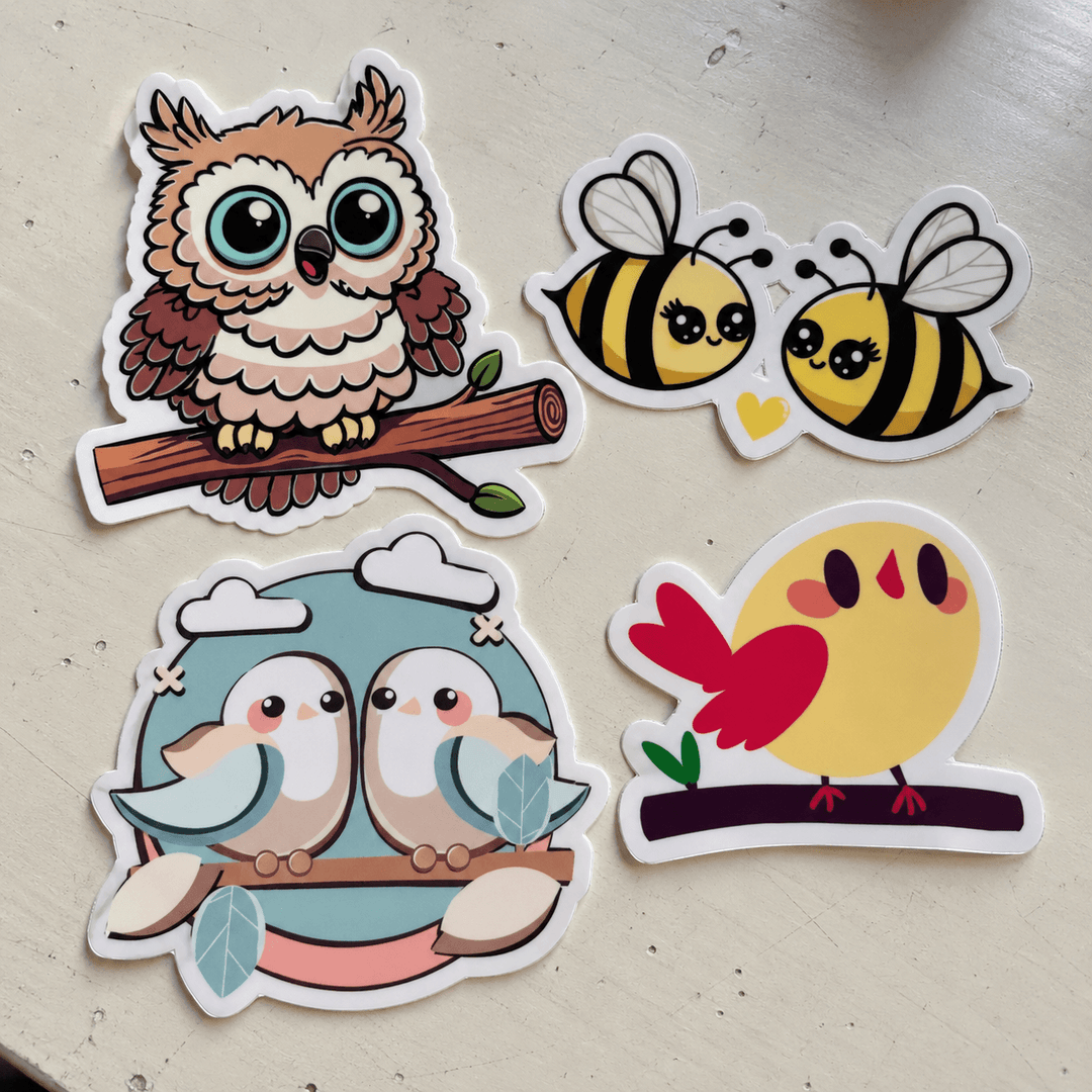 Four cartoon animal stickers arranged on a light beige surface: an owl on a branch, two bees facing each other, two birds hugging, and a yellow bird with a red tail. The stickers have white borders and are photographed from above.