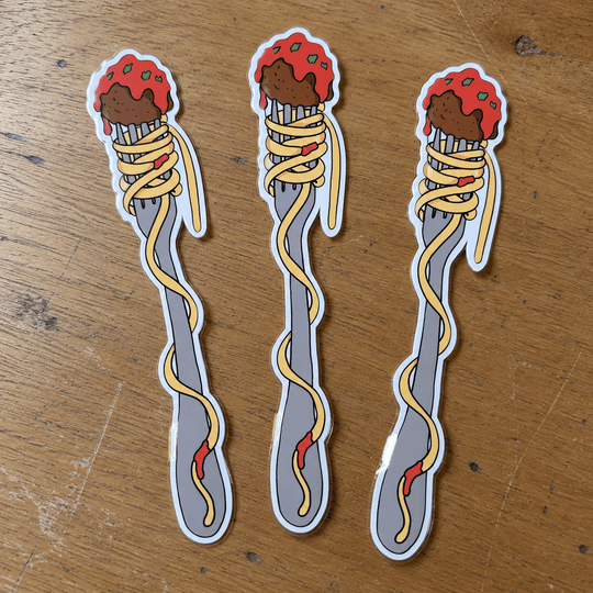 Three identical die-cut stickers of a fork wrapped in spaghetti with meatballs, displayed on a wooden tabletop.