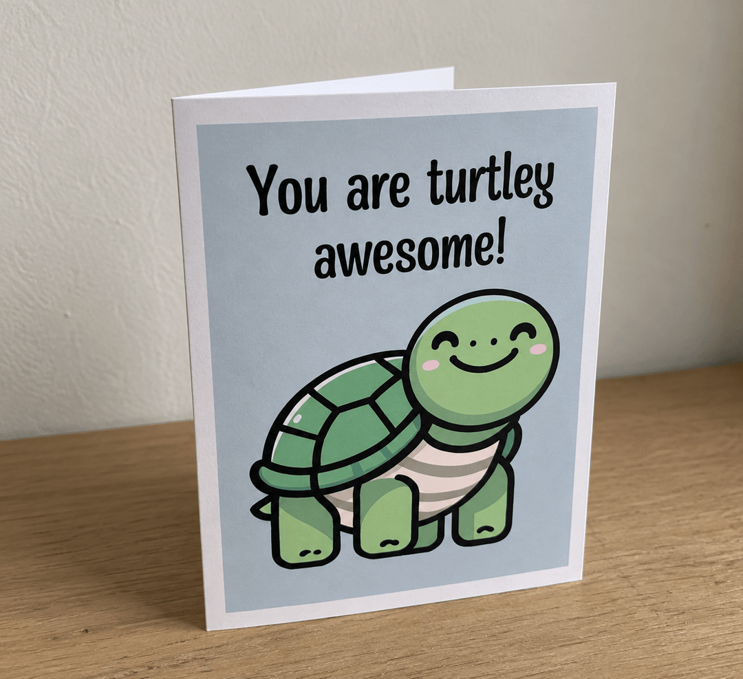 A folded greeting card standing upright on a wooden surface against a light beige wall. The card has a white border and a light blue center area featuring a cute green cartoon turtle and the text &