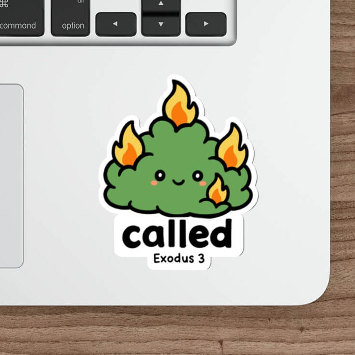 A die-cut sticker featuring a cute green cartoon cloud with orange flames and the text 'called Exodus 3' below it, shown applied to the lower part of a silver laptop on a wooden desk next to a mouse and stylus.