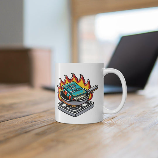 Quirky white ceramic mug featuring a cartoon book engulfed in flames, with the clever text 'Cook the Books,' making it a fun gift for book lovers