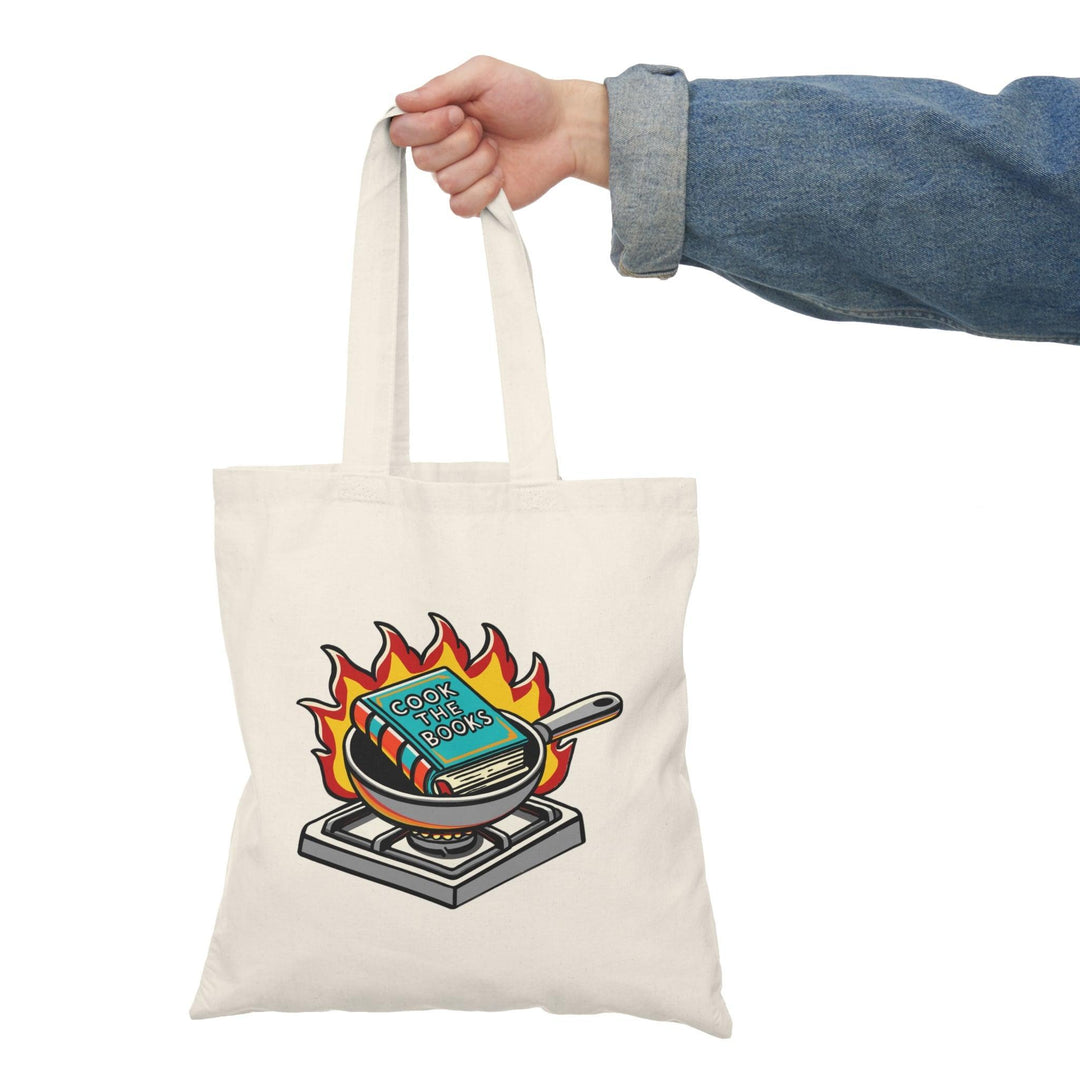 Tote bag featuring a whimsical illustration of a chef's hat resting on an open cookbook, accompanied by playful graphics and the phrase 'Cook the Book.' The vibrant design and fun colors make it an ideal accessory for food lovers and culinary enthusiasts, perfect for carrying groceries or your favorite recipes.