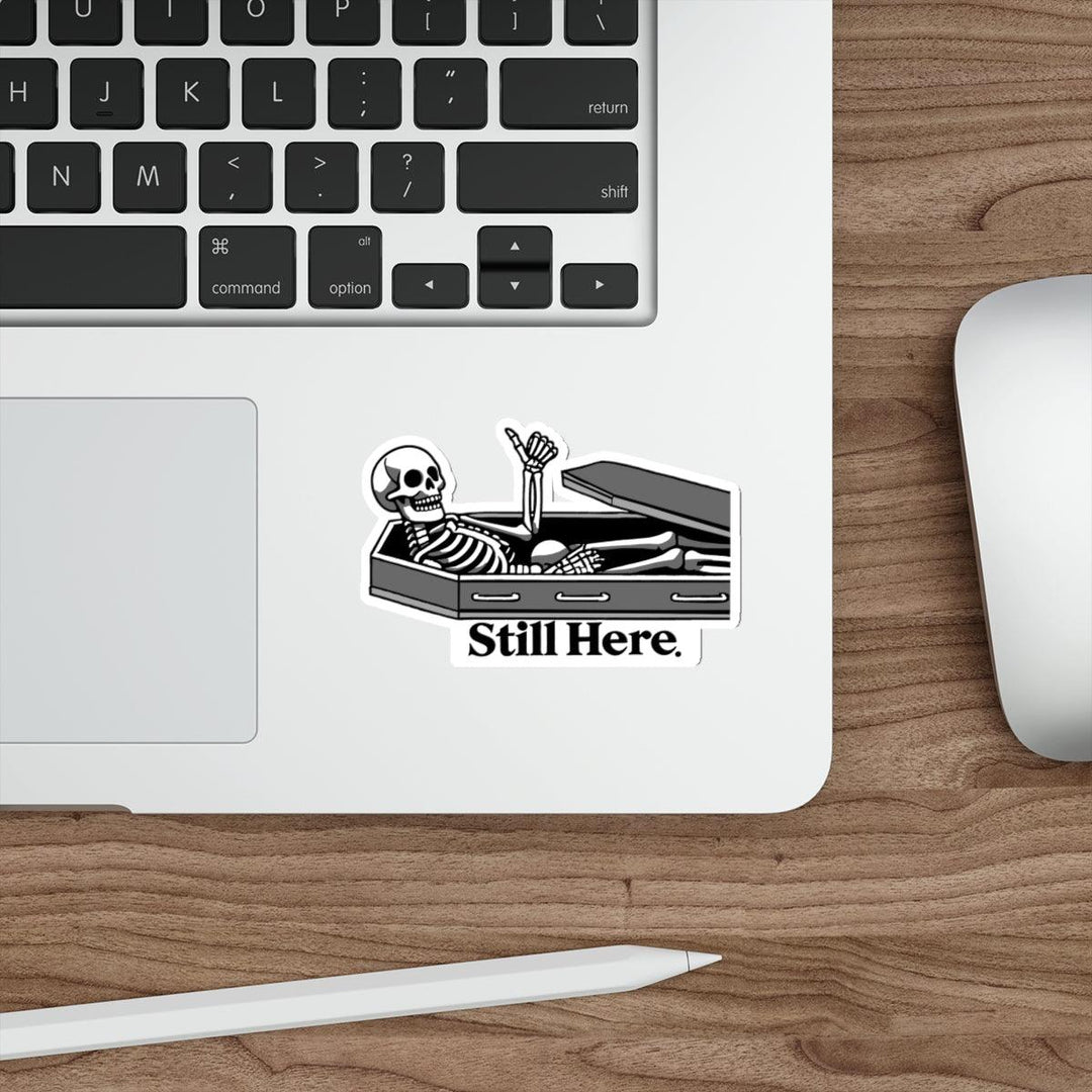 Still Here Skeleton Waterproof Sticker: A lounging skeleton with the phrase "Still Here," representing resilience with a humorous undertone, great for Halloween or everyday use. Baby Keo.
